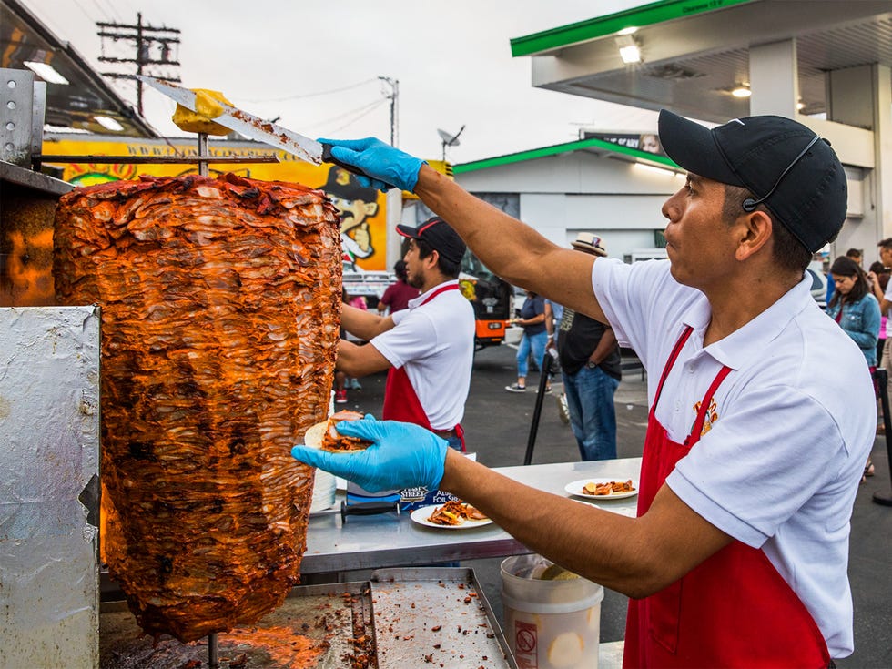 A worker slices off a piece of pineapple atop a spit of al pastor marinated pork on a vertical grill at Leo’s Taco Truck.