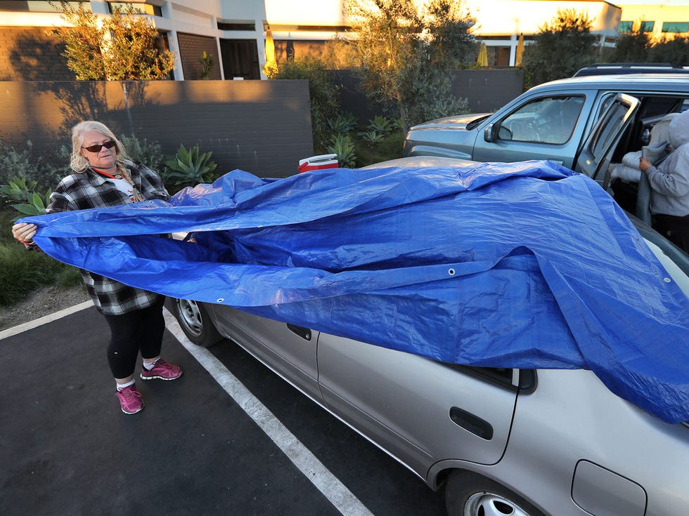 As the sun comes up in San Diego's Kearny Mesa area, Kathy Jones removes the tarp she used to cover the windows of her Toyota where she slept last night. Many of the homeless who stay overnight in the parking lot cover their vehicle for privacy.
