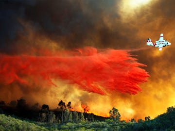 A Cal Fire airplane drops retardant on a large hilltop home that caught fire during a 2014 wildfire in San Marcos.