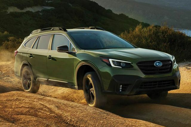 subaru outback driving on an off road mountain trail with mountains and water in the background