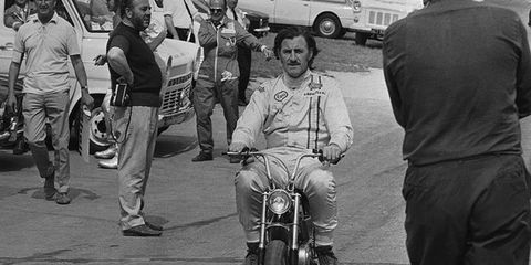 Graham Hill rides his motorcycle through the crowd.