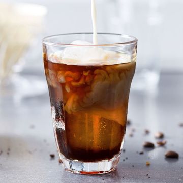 pouring milk creamer into glass of homemade cold brew coffee in kitchen