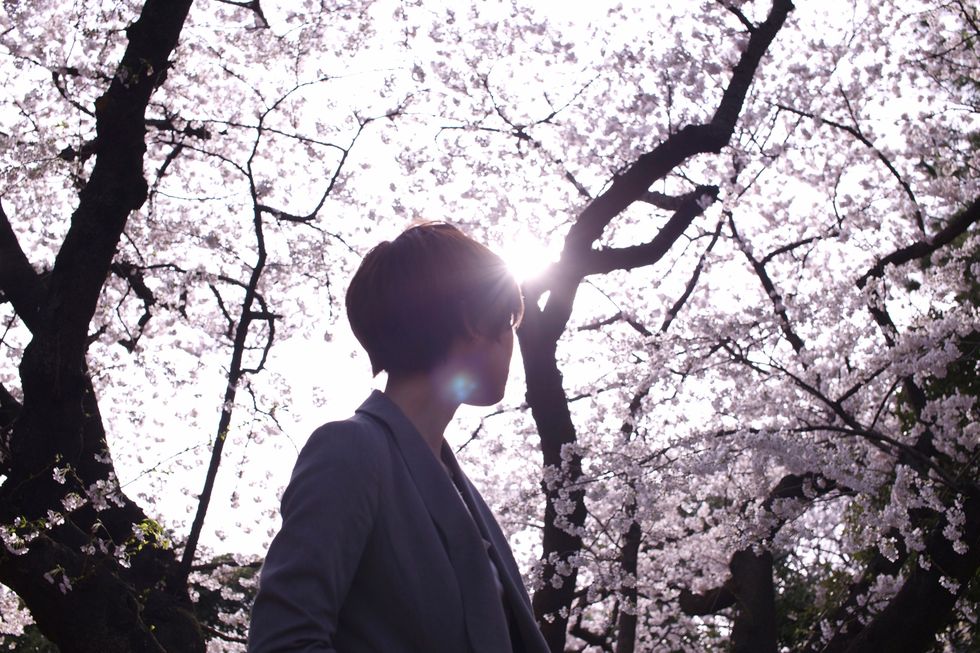 Woman is looking up at sky in front of cherry blossom.