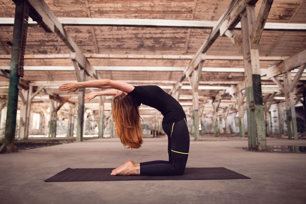 Woman practicing yoga in abandoned warehouse. She is redhead and wearing black tights and t-shirt and looks very attractive, with slim body and perfect skin.
