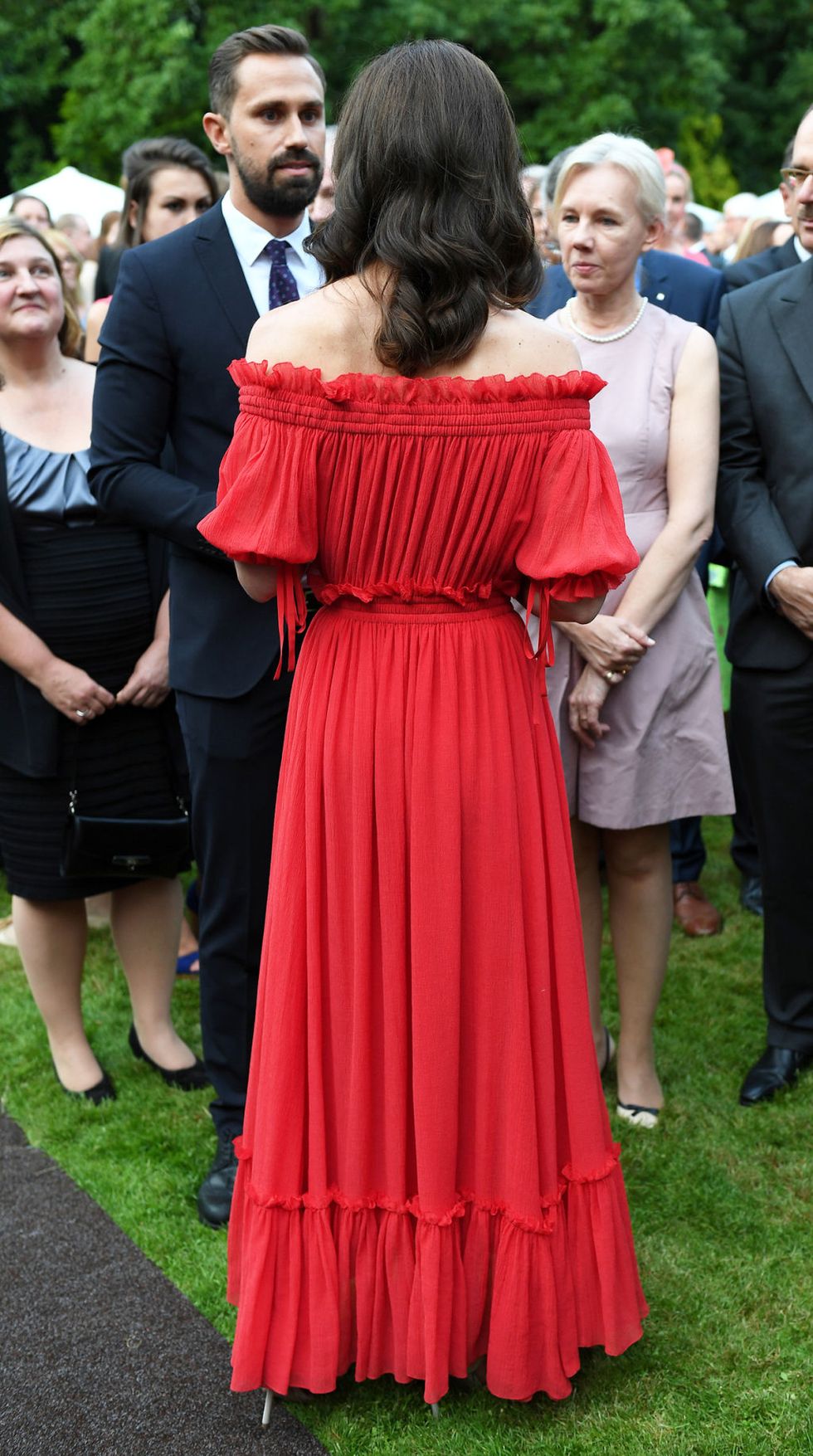 L'abito lungo rosso di Kate Middleton ti riporta a un'eleganza di altri tempi, quella degli anni 70: le spalle scoperte, il nido d'ape e le maniche a sbuffo sono i dettagli da copiare che fanno di questo abito un esempio perfetto da indossare a un evento elegante.