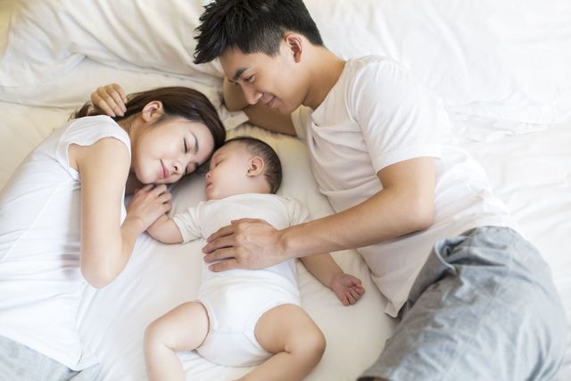 添い寝する赤ちゃんと若い夫婦／赤ちゃんを見て微笑む男性
