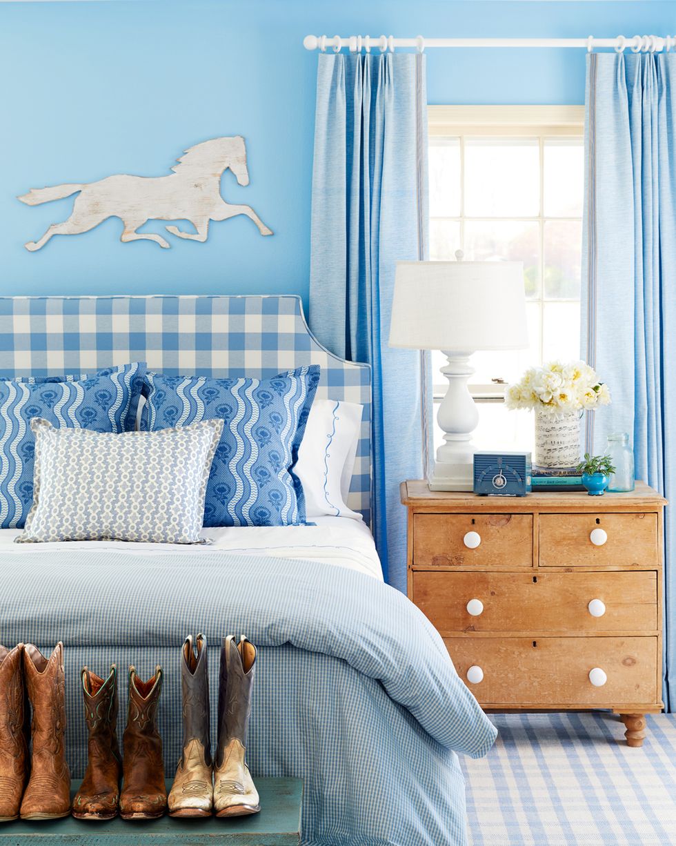 blue bedroom with blue checked headboard and bench with cowboy boots at the end