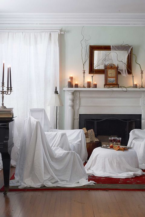 living room decorated for halloween with cobwebs, candles, and sheets over the furniture to make it look abandoned