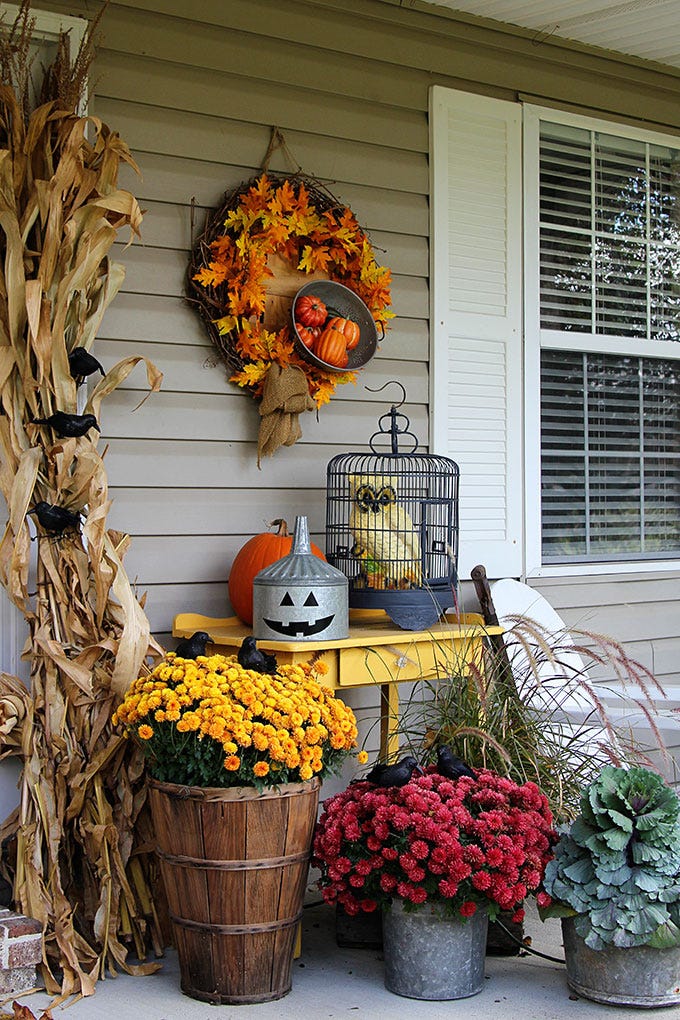 fall porch decor with potted mums, ornamental cabbage, faux crows roosting in corn husks, oil tin with jack o lantern face