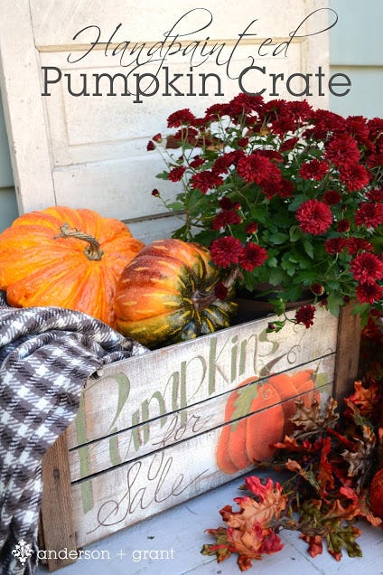 painted wood crated that says pumpkins for sale filled with gourds, plaid throw blanket, potted red flowers for fall