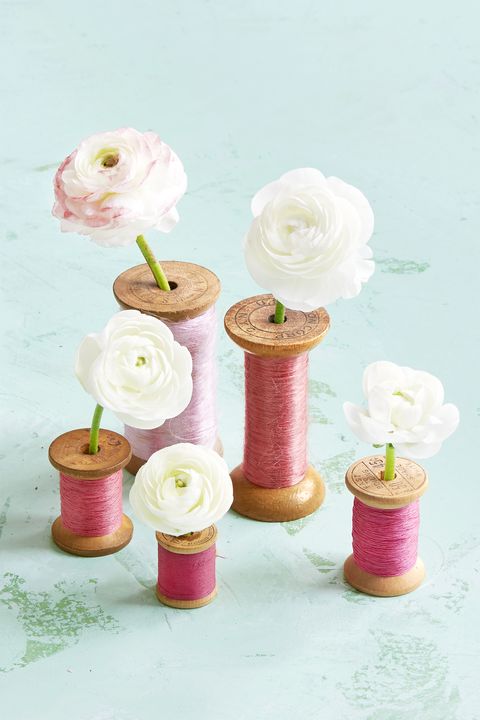 assorted sizes of vintage wooden spools of pink thread turned into bud vases and holding individual blooms of white ranunculus