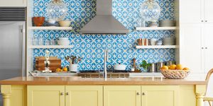 kitchen with yellow painted island and blue and white tile backsplash that extends to the ceiling behind open shelves and stainless steel hood