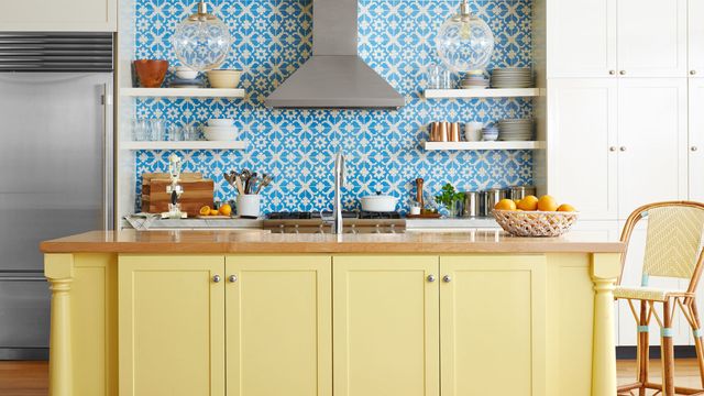 kitchen with yellow painted island and blue and white tile backsplash that extends to the ceiling behind open shelves and stainless steel hood