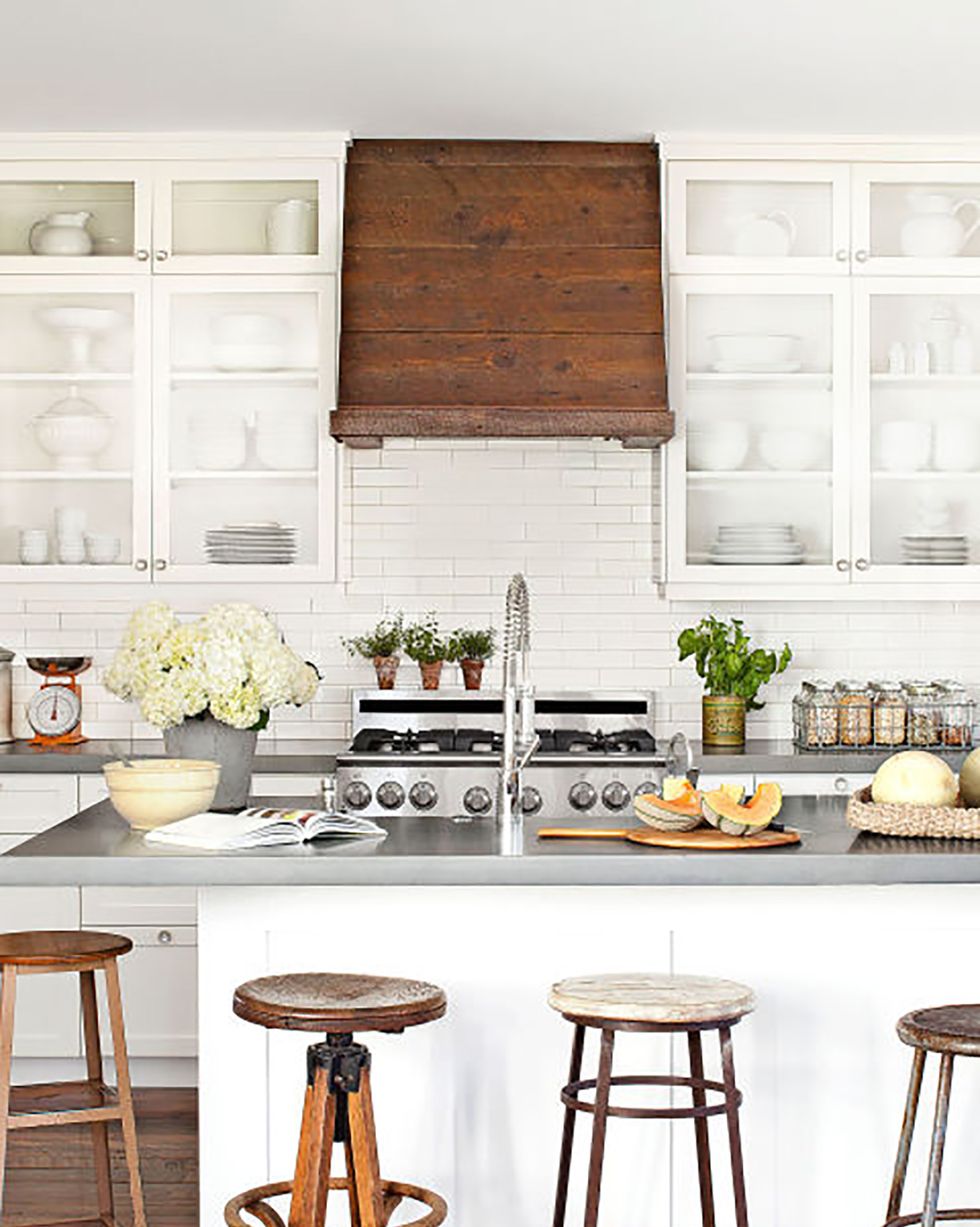 an all white farmhouse kitchen with a warm wood range hood and barstools that are mismatched