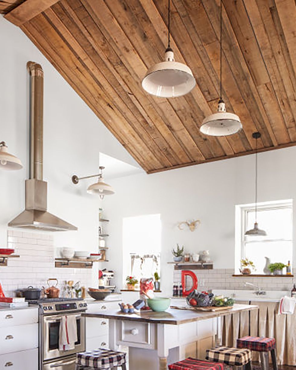 a farmhouse kitchen that is mostly white but has reclaimed lighting and an island with a wood top and barstools with plaid covers