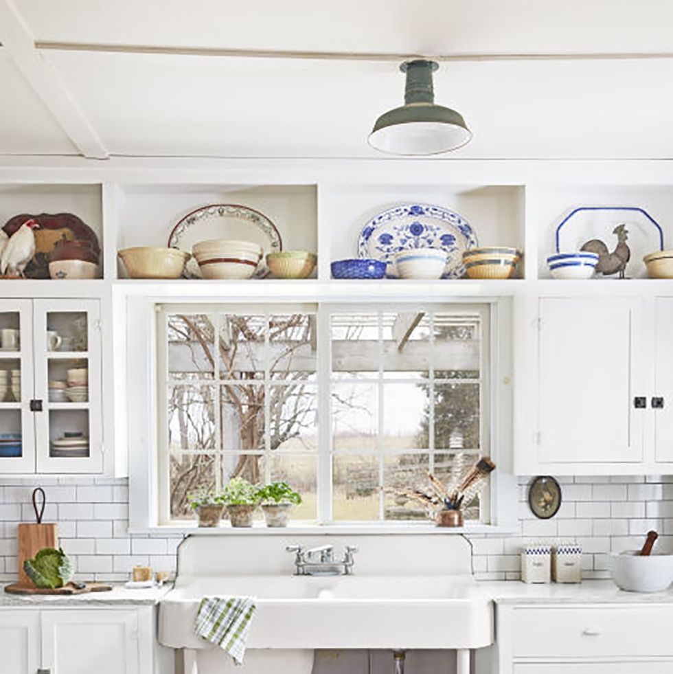 a white antique sink is nestled between two white cabinets and under a window in a farmhouse kitchen