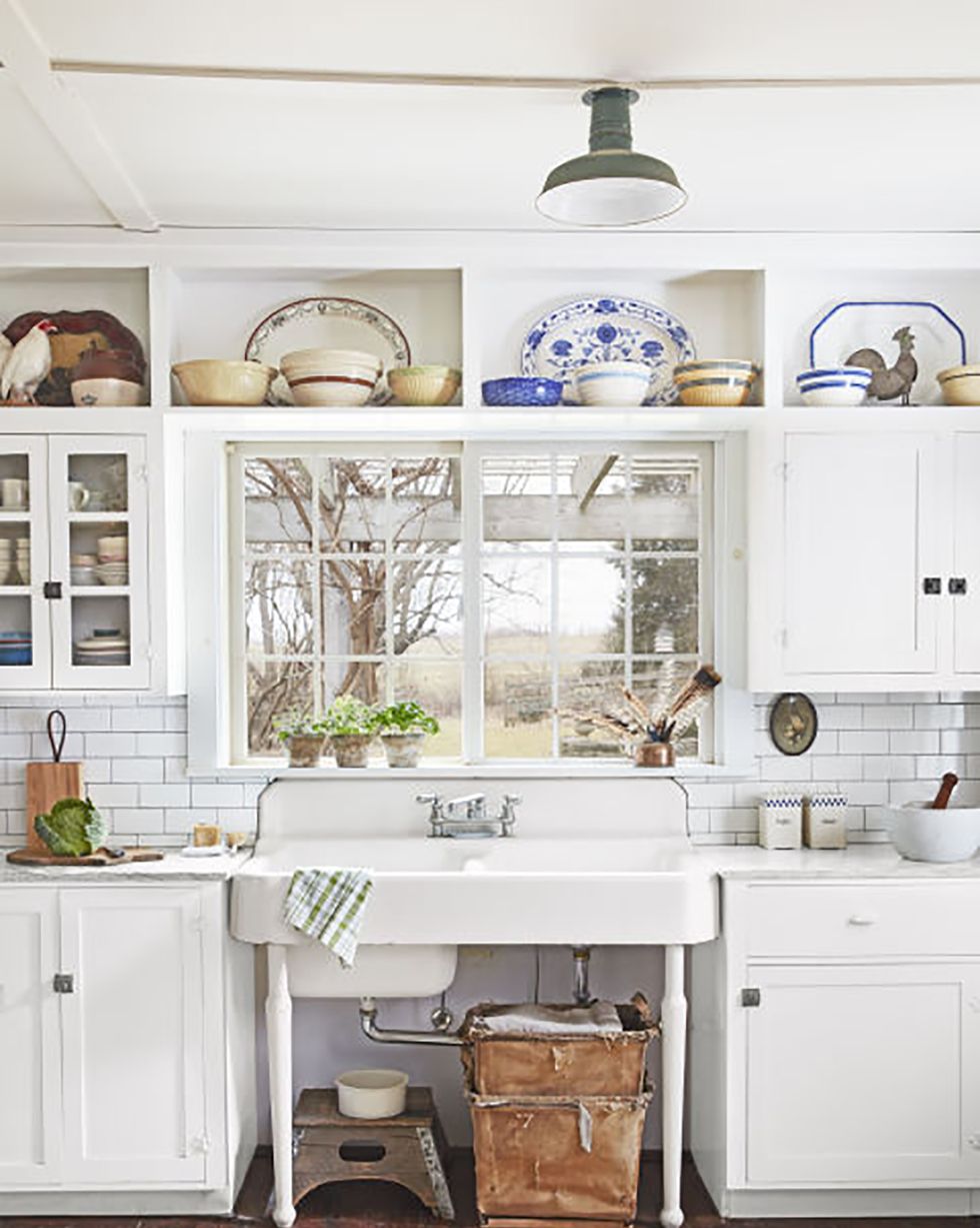 a white antique sink is nestled between two white cabinets and under a window in a farmhouse kitchen