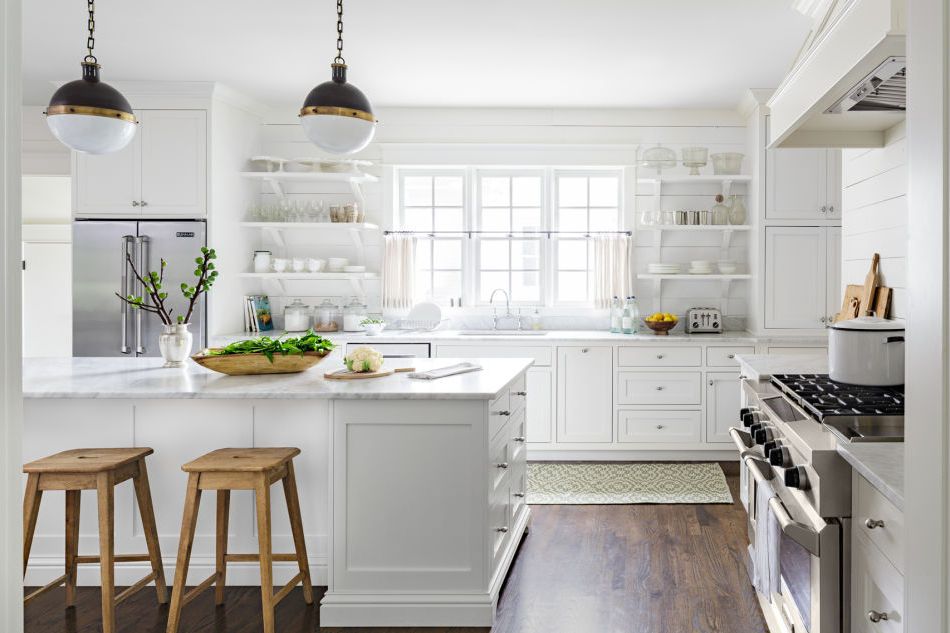 an all white farmhouse kitchen that has a big island and stainless steel appliances