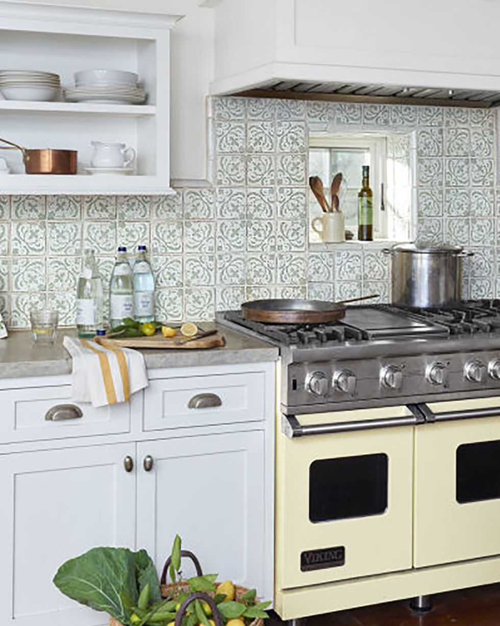 a butter yellow stove sits against a white and green tile backsplash and white cabinets and concrete countertops