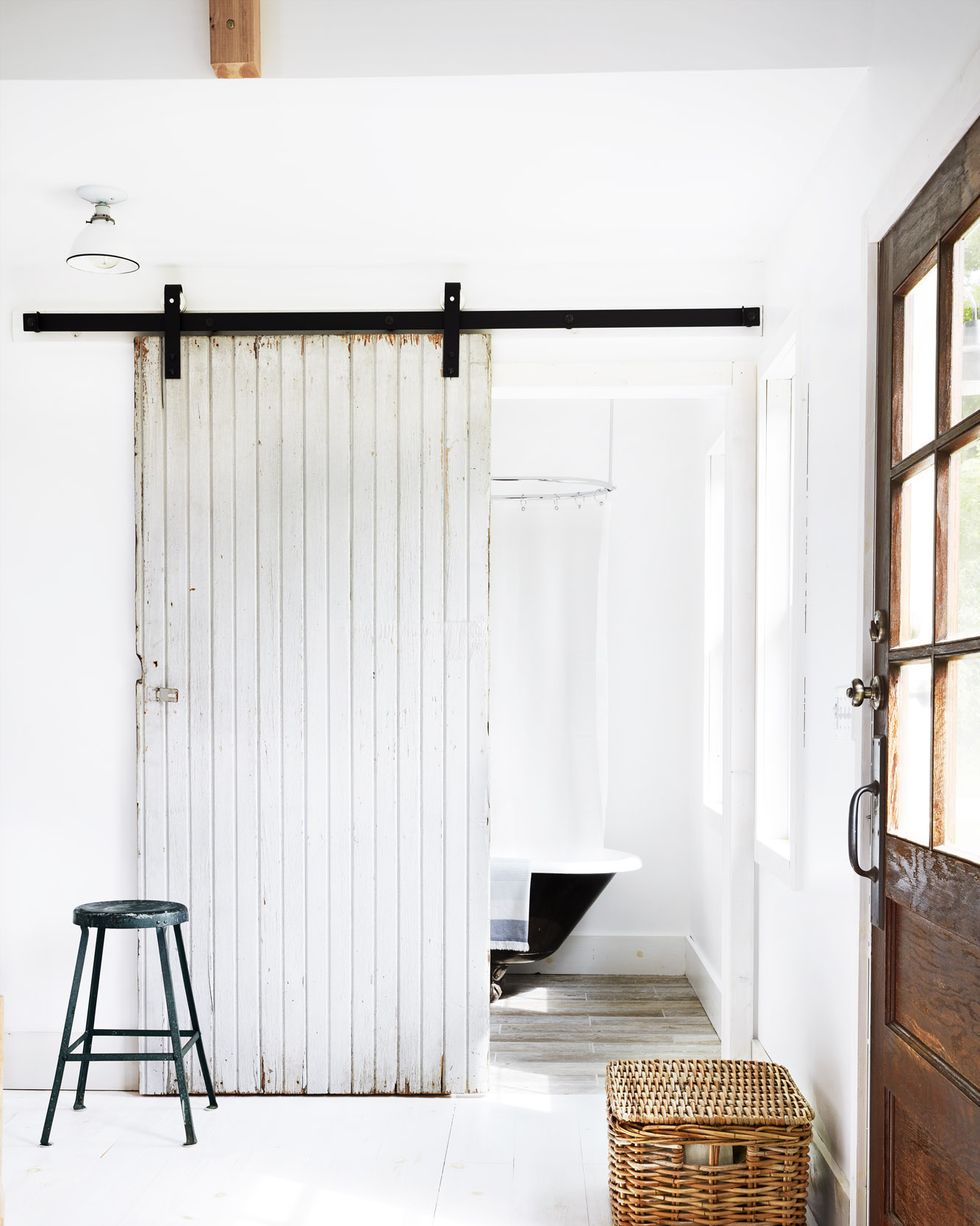 a sliding white barn door leading to a bathroom with a black clawfoot tub