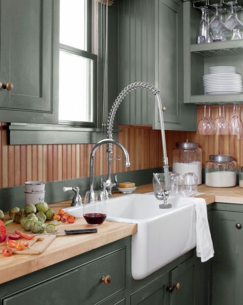a corner of a kitchen that has green cabinets and wood countertops and a wood backsplash too