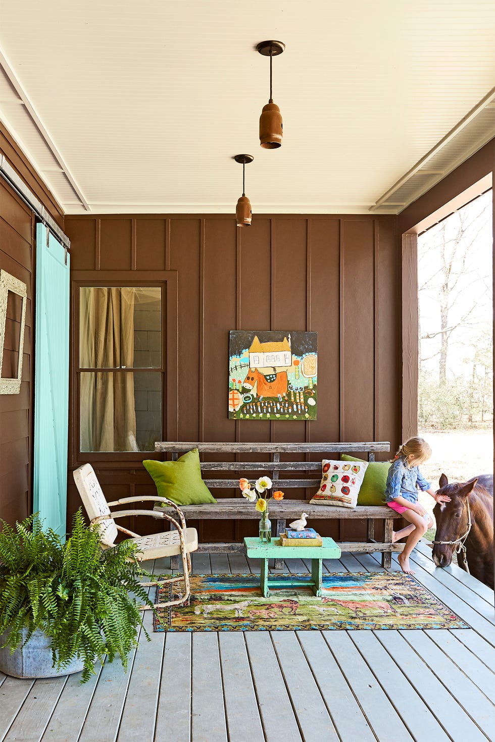 porch with brown walls, rustic bench with green pillows, horse themed decor, and a girl petting a horse