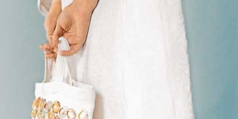 woman in white linen dress holding white tote bag with seashells sewn on