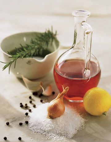 vinegar in a glass jug next to a lemon and garlic and herbs