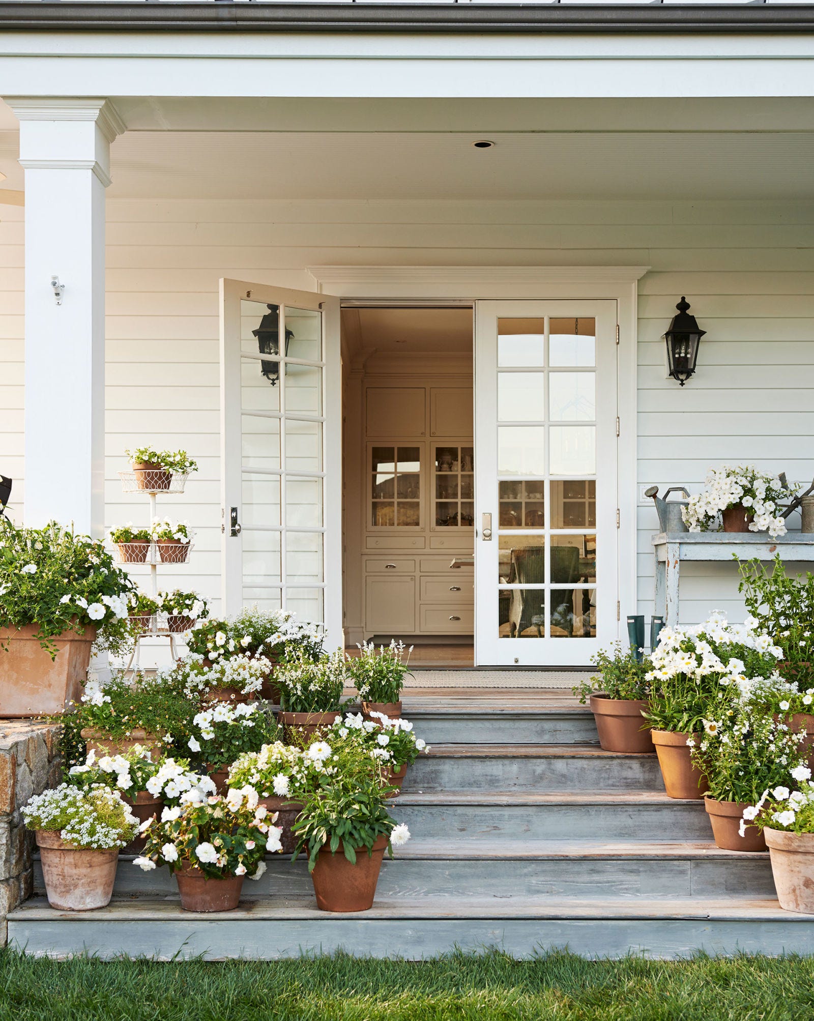 Charming back porch off farmhouse kitchen with wide steps massed with terracotta pots of flowers. #porch #decoratingideas #steps #farmhouse