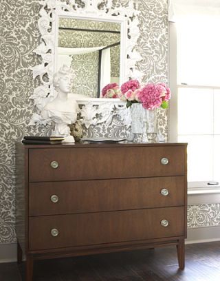 white mirror above brown dresser with white statue and flowers
