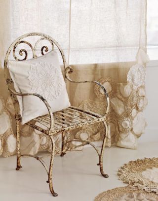 a cream iron chair by a window, with doily-embellished drapes and an off-white pillow with doily sewn on