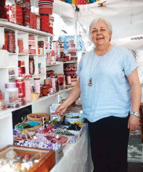 susan gower standing alongside shelves of red trim and ribbons