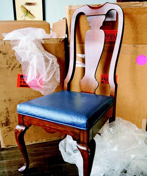 a wooden chair with pleather cushion surrounded by boxes and bubble wrap
