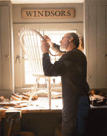 man working on a windsor chair on a table