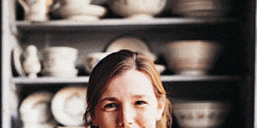 woman smiling and sitting in front of shelves of ceramic ware