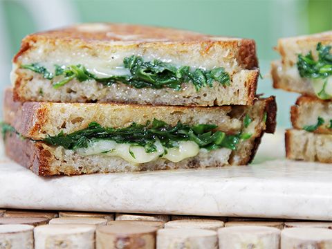 gourmet grilled cheese filled with melted white cheese and greens on white stone cutting board