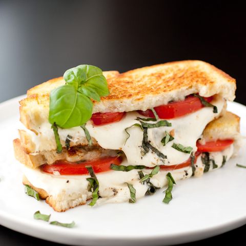 stacked grilled cheese halves filled with shedded basil, sliced tomato, melted mozzarella on white plate