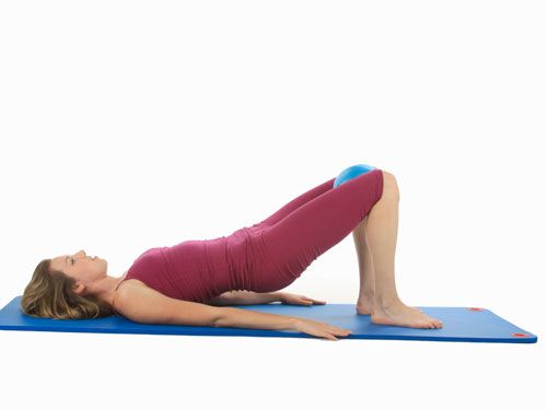 Lie on your back, arms by your sides, knees bent. Place a small exercise ball or rolled-up towel between your knees. Squeeze the ball and your glutes as you lift your hips up to the ceiling into bridge position. Hold for six seconds, then slowly lower. Repeat 10 times.