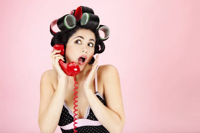 Woman in curlers on the phone looking shocked