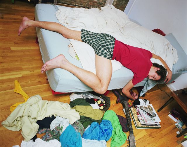 Young man lying on a bed with clothes scattered over the floor