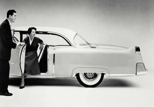 Man holding 1950s car door open for woman