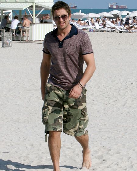 We're not sure how, but gorgeous Gerard has managed to pull off this dodgy ensemble of combat shorts and a striped t-shirt, but still look heartbreakingly hot on Miami beach, although we'd prefer him out of those clothes!  <br />
