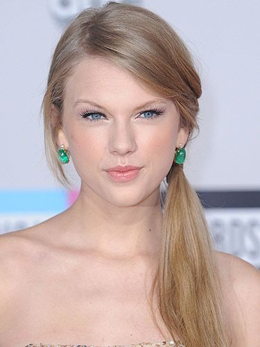 <p>For a dramatic long side ponytail like Taylor Swift's you need to have a lot of hair, or you can use a hairpiece to get the look. Gather all your hair to the side of your head just below the ear and secure with a strong snag-free elastic. Next, attach your faux pony if you're using one.  If not simply separate your hair into two sections, one smaller than the other, and twist the smaller section around the base of your ponytail (this will hide the join whether you are using a faux pony or not) and secure with grips. Use a straightening iron on the hair in the ponytail to get it super sleek. Good luck!</p>