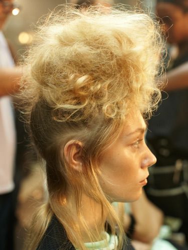 <p><strong>The hair look:</strong> Styled by global ghd creative director Sam McKnight and his team, hair was reminiscent of Greek statues with major backcombing for tall statuesque silhouettes.</p>
<p><strong>Get the look:</strong> 1) Using the ghd tail comb, take out the hairline from temple to temple, leaving a soft airy section around the hairline. 2) Gather all the remaining hair into a high pony at the top of the head, using the ghd oval dressing brush to smooth for a sleek finish. Secure with an elastic band. 3) Take small sections of hair from the pony at a time and wrap around one finger. Once wrapped, gently release your finger holding the curl in place. Using the ghd eclipse styler, close onto the curl and hold for approximately five seconds, then pin up and leave to cool. 4) Once repeated throughout the whole ponytail, release the pins and brush through the hair to free all movement and soften the curls. Backcomb at the roots using the ghd tail comb to create extra volume and give a light fluffy texture to the hair. 5) Taking small sections, pin and tease the hair forward and upwards, creating a tiara shaped head-dress with the hair piled high. 6) Spray the whole style with hairspray to the point that hair is almost wet and wrap with a hairnet. Ensure the sides are kept tight to the head and the front elevated to create the tiara shape. Next, use the ghd air hairdryer to set the shape in place, making use of the cool shot button and run the ghd eclipse styler over the remaining hair underneath creating a smooth, wispy finish.</p>