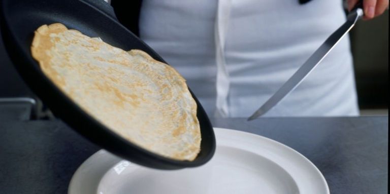 Classic pancakes on frying pan tilted towards plate