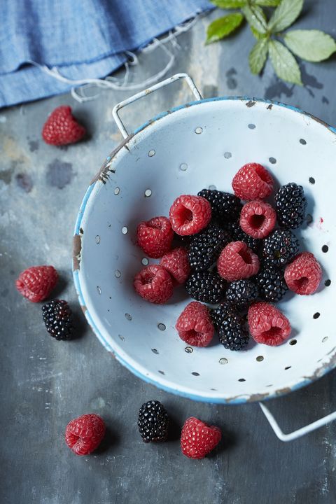 Blackberries and raspberries in sieve on rustic table
