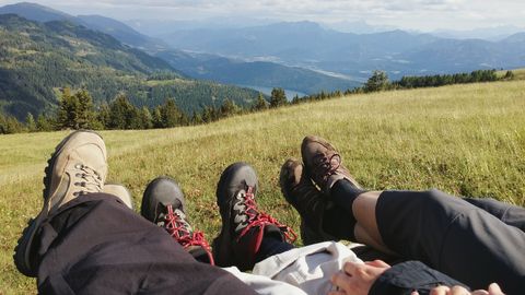 Up close image of three pairs of feet in walking shoes on hillside in countryside