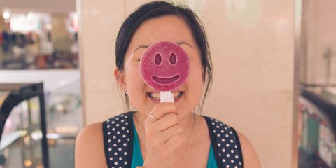 Happy Young Woman Holding Smiley Face Lollipop At Restaurant