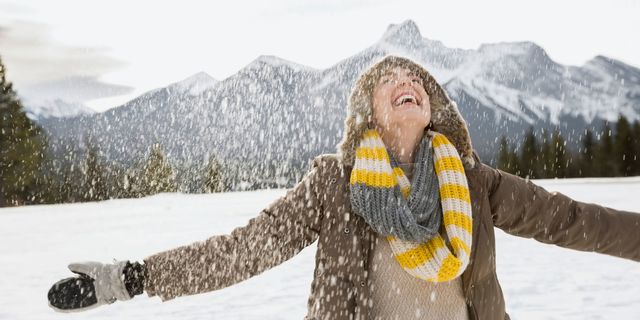 Snow falling around happy woman with arms outstretched