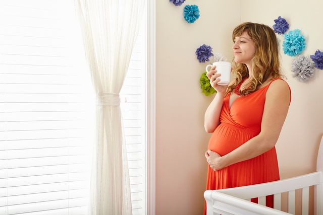 Pregnant woman in nursery holding coffee